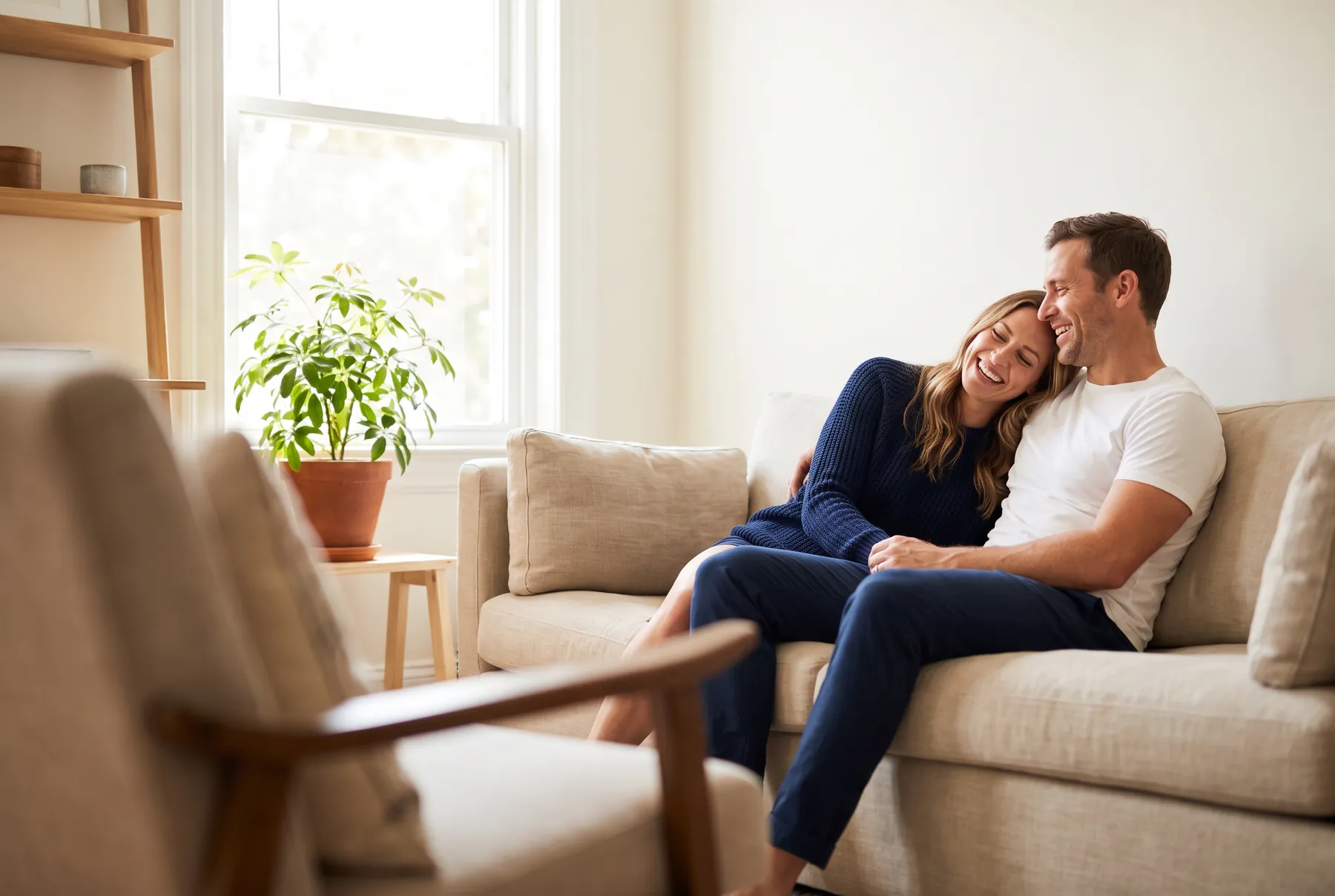 Couple in their thirties laughing together on a sofa at home